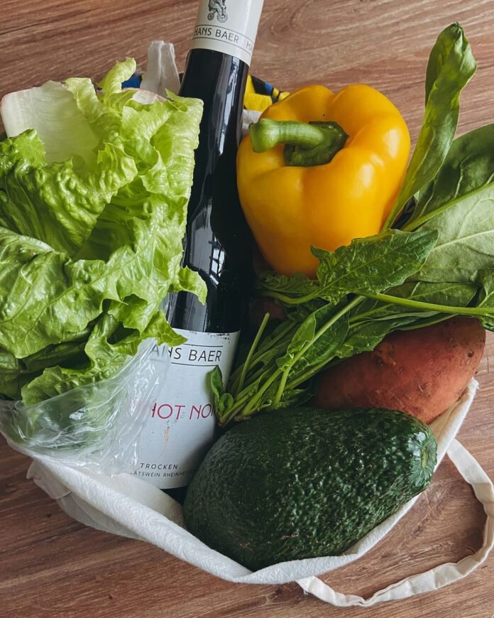 A vibrant collection of fresh vegetables with a wine bottle on a wooden table.