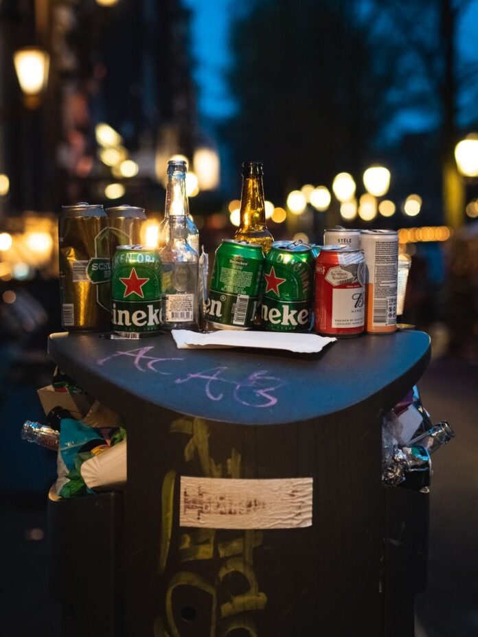 Photo by Kai Pro A vibrant street scene depicting discarded bottles and cans on a city trash can at night.
