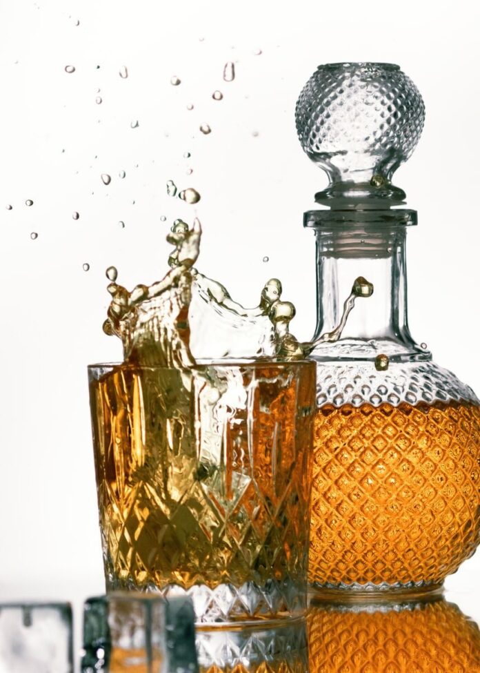 Photo by Katja B A captivating image of whiskey splashing in a crystal glass with a detailed decanter in the background.