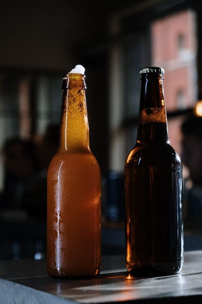 Photo by cottonbro studio Two beer bottles on a table with soft bokeh, perfect for beverage themes.