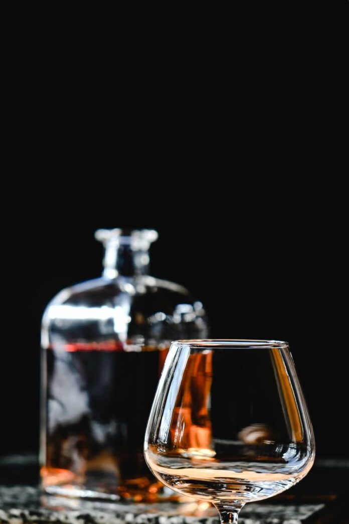 Close-up of a whiskey bottle and glass reflecting on a marble surface with a dark background.